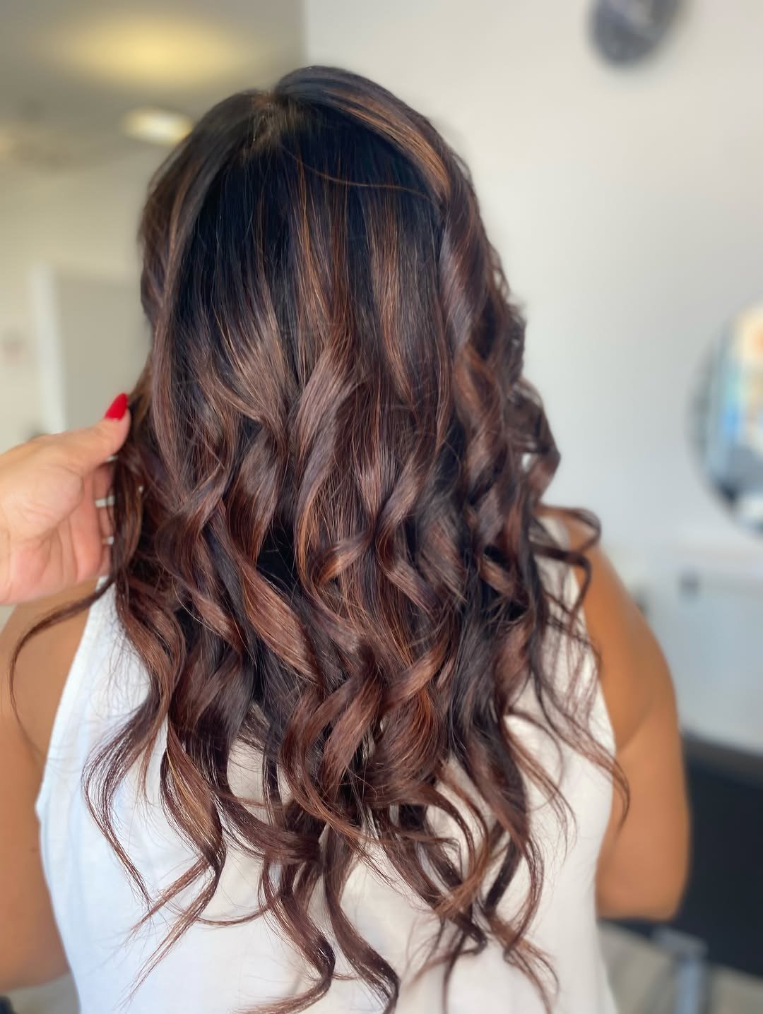 Cabelo castanho escuro com balayage acobreado em caracóis, visto de costas