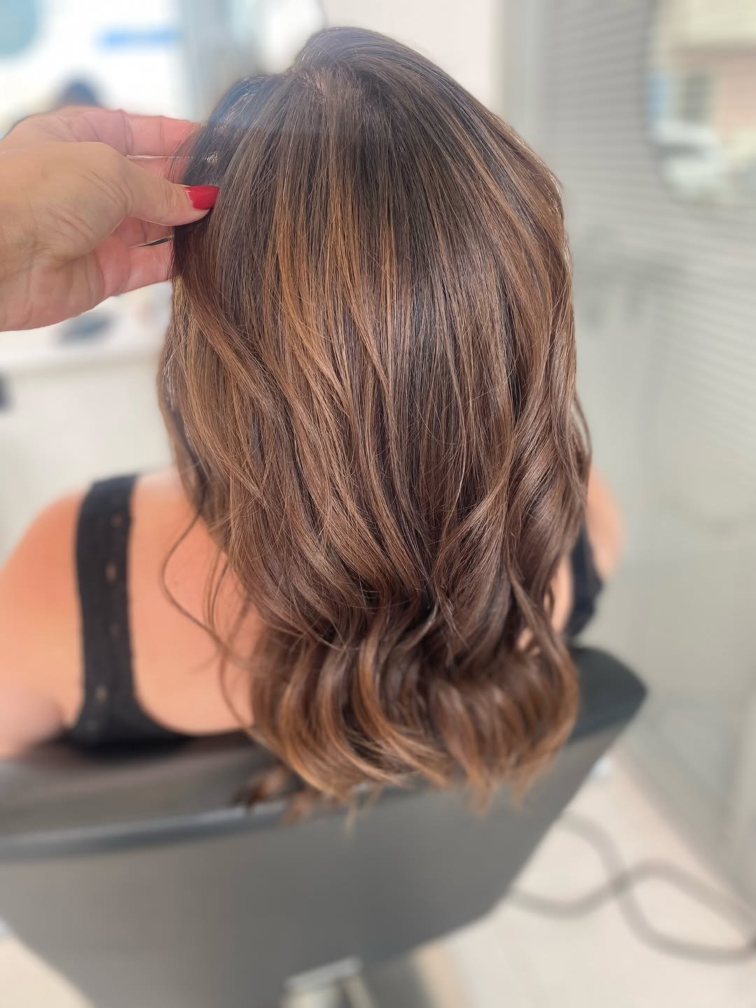 Cabelo castanho médio com reflexos quentes, visto de costas, com uma mão a levantar a raiz