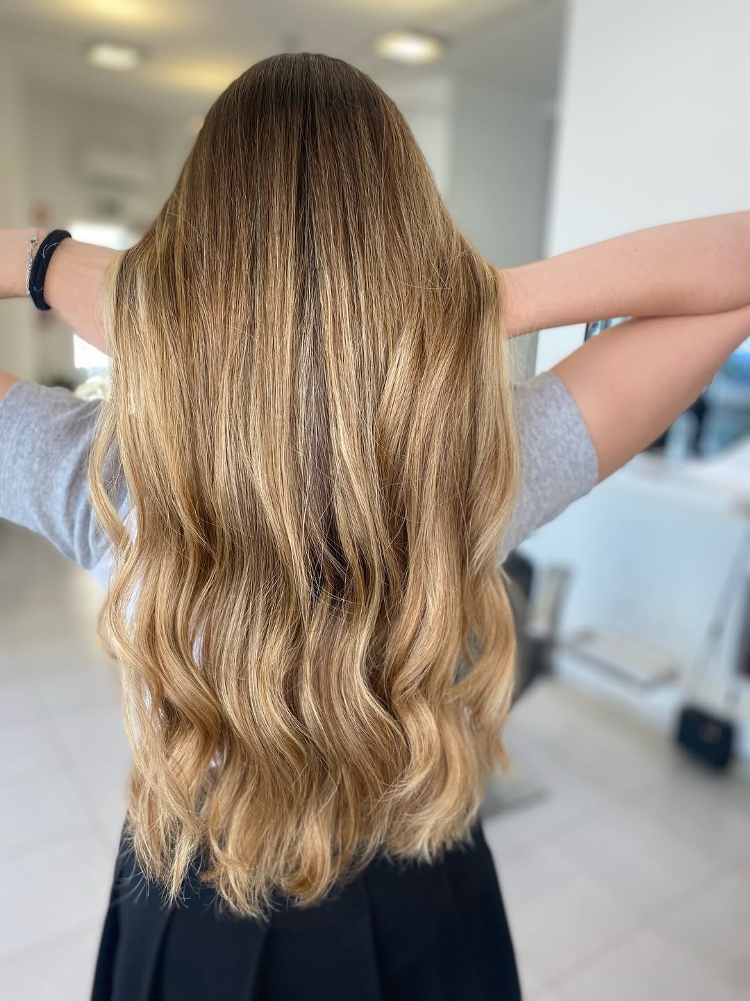 Cabelo comprido loiro mel com balayage e ondas, visto de costas no salão